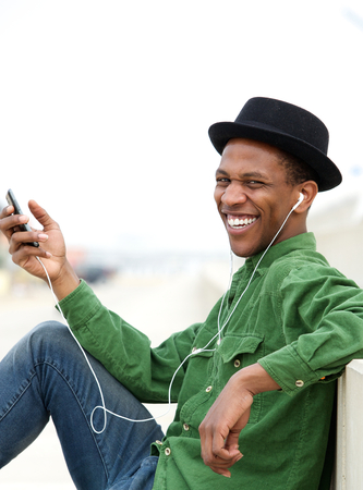 Portrait of a young man smiling outdoors with mobile phone and earphonesの写真素材