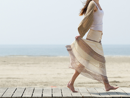 One female walking at the beach barefoot with dress