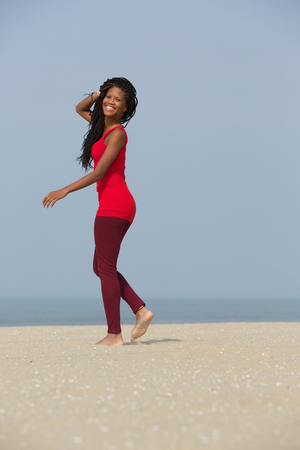 Full length portrait of a cheerful african american woman walking on the beachの写真素材