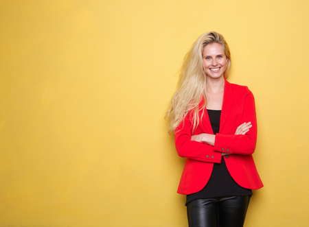 Portrait of a beautiful young woman in red jacket smiling on yellow backgroundの写真素材