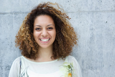 Close up portrait of a beautiful young woman with curly hair smiling outdoorsの写真素材