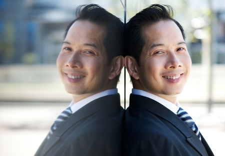 Close up portrait of a smiling businessman leaning on wall with reflection の写真素材