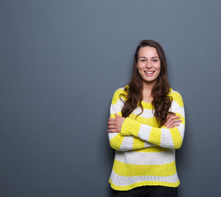 Portrait of a beautiful young brunette woman smiling with arms crossed on gray backgroundの写真素材