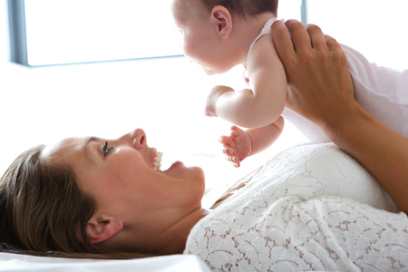 Close up portrait of a smiling mother holding baby in bedの写真素材