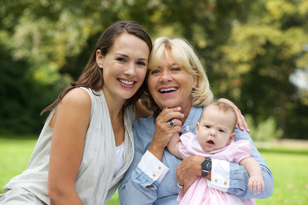Close up portrait of a smiling mother sitting outdoors with grandmother and child
