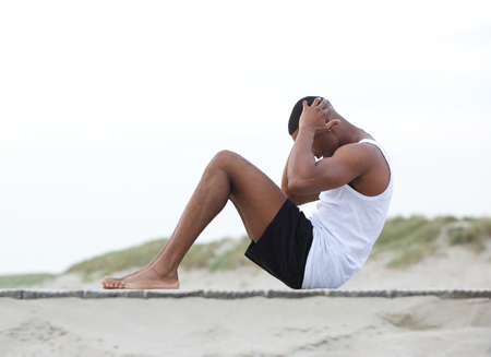 Side view portrait of a young man exercising on the beach doing sit upsの写真素材