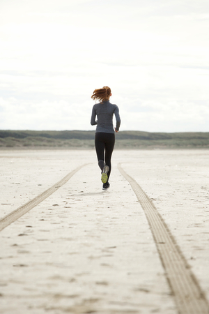 Rear view portrait young woman running at the beachの写真素材
