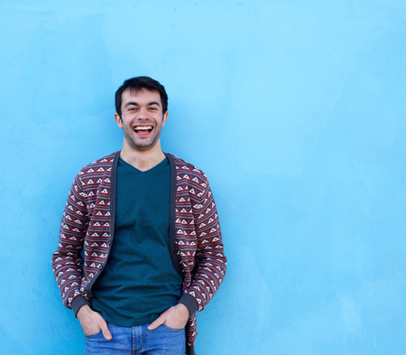 Portrait of a young man laughing against blue background