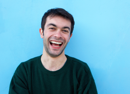 Close up portrait of a cheerful young man laughing against blue backgroundの写真素材