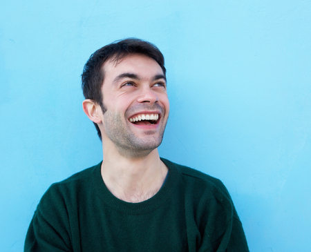 Close up portrait of a cheerful young man smiling against blue backgroundの写真素材
