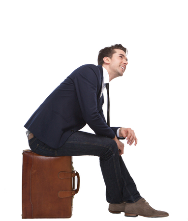 Portrait of a cheerful business man sitting on suitcase on isolated white backgroundの写真素材