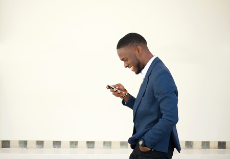 Side portrait of a smiling businessman walking and sending text message on mobile phoneの写真素材