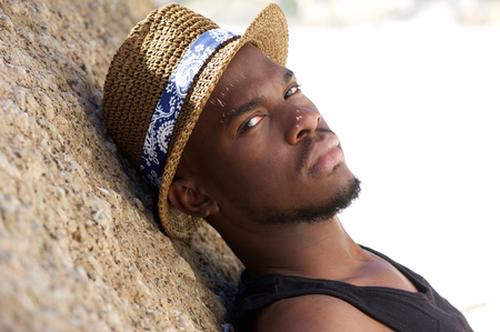 Close up portrait of an attractive african american man relaxing outdoors with summer hatの写真素材
