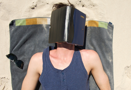 Portrait of young man sleeping on beach with book covering faceの写真素材