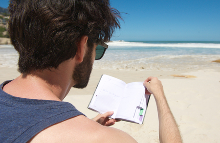 Close up portrait from behind of a young man reading book at the beachの写真素材