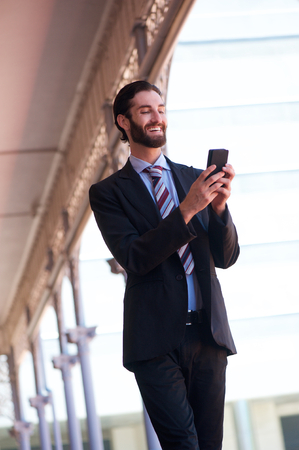Portrait of a smiling businessman sending text message on cell phoneの写真素材