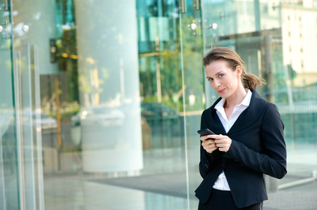 Portrait of an attractive business woman walking outside with mobile phoneの写真素材
