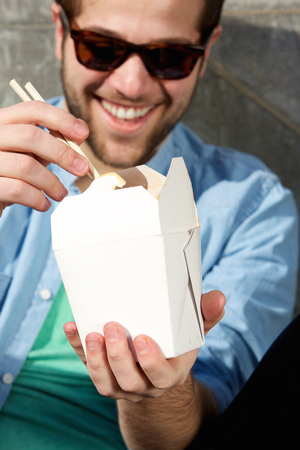 Close up portrait of a cool guy eating takeaway food with chopsticksの写真素材