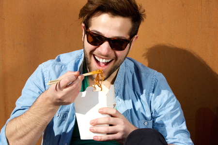 Close up portrait of a young man laughing and eating noodles with chopsticksの写真素材