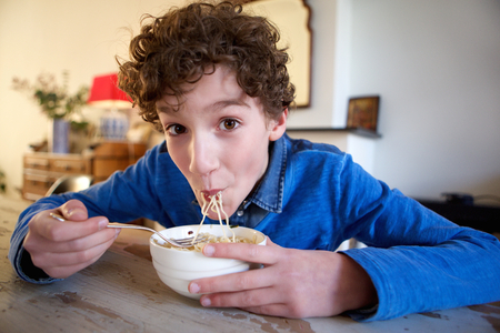 Portrait of a happy boy eating noodles at homeの写真素材