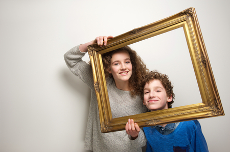 Portrait of a happy brother and sister holding picture frameの写真素材