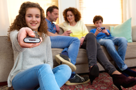 Portrait of a happy girl holding remote control with family in the background