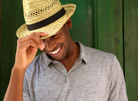 Close up portrait of a happy young man laughing with hat and looking downの写真素材