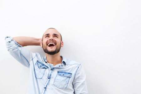 Close up laughing guy looking up with hand behind head standing against white backgroundの写真素材