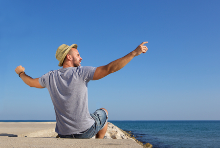 Portrait from behind of a man sitting by the sea with arms spread openの写真素材