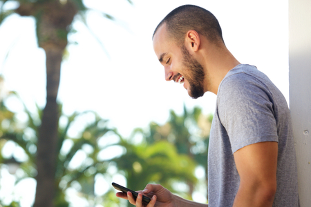 Portrait of a cheerful young man reading text message on mobile phoneの写真素材