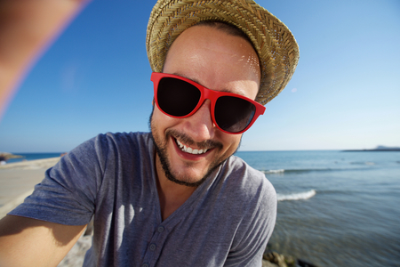 Cheerful young man with hat at the beach taking selfieの写真素材