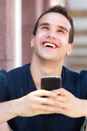 Close up portrait of a smiling man holding mobile phone and looking upの写真素材