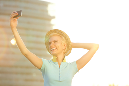 Portrait of a smiling young fashion woman with hat taking selfieの写真素材