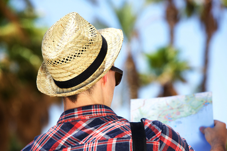 Rear portrait of a male tourist with hat looking at map on vacationの写真素材