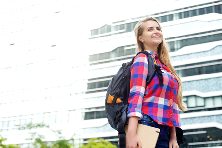 Portrait of a smiling female student walking outside with bag and book