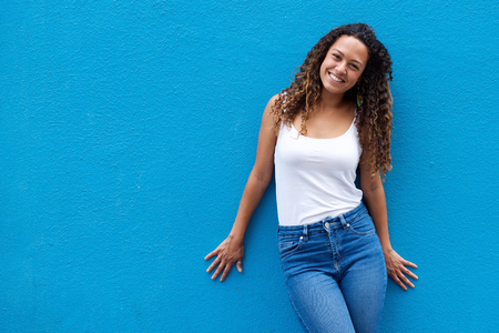 Portrait of smiling young woman standing against a blue wall looking at cameraの写真素材