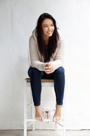 Full length portrait of a smiling young woman sitting on chairの写真素材