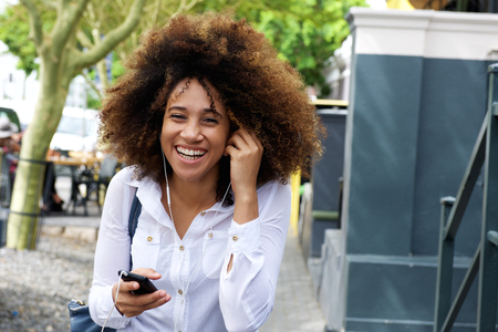 Portrait of laughing young woman walking with cellphone and earphonesの写真素材
