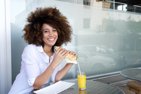 Portrait of young african american woman holding sandwich at cafe restaurantの写真素材