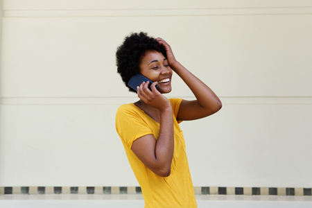 Portrait of young black woman talking on mobile phone and smiling with her hand on headの写真素材