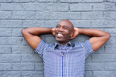 Close up portrait of smiling black man standing with his hands behind head against a gray wallの写真素材