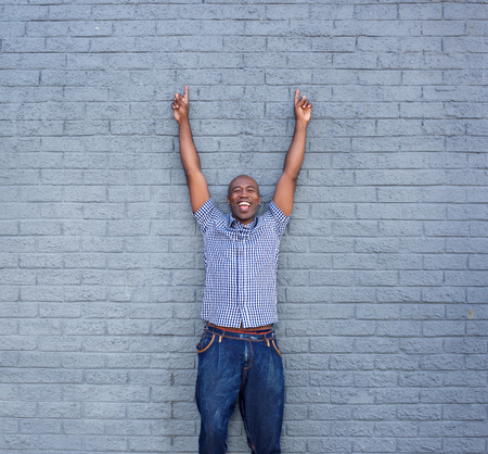 Portrait of cheerful man standing with his hands raised against a gray wall