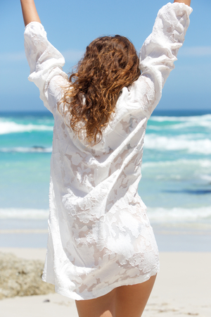 Portrait of back of young woman with arms raised at the beachの写真素材