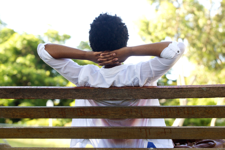 Rear portrait of young woman relaxing on park bench with hands behind headの写真素材