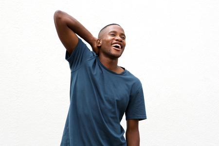 Portrait of a cheerful young african man standing with hand behind head against white wallの写真素材