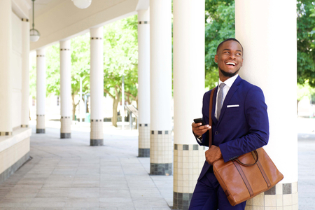 Portrait of a smiling young businessman standing outdoors leaning with cell phoneの写真素材