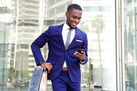 Portrait of young african businessman standing in the city with mobile phoneの写真素材