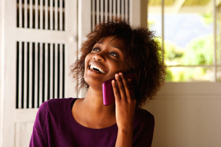 Close up portrait of a young black woman smiling with cell phoneの写真素材
