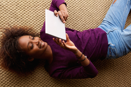 Portrait from above smiling black woman lying down with digital tabletの写真素材