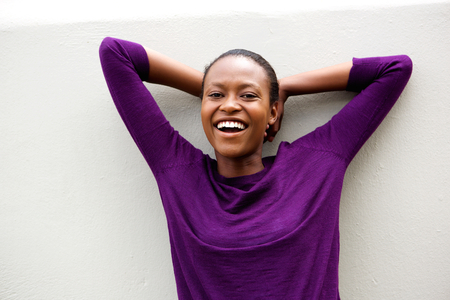 Portrait of cheerful young african woman standing with her hands behind head against white backgroundの写真素材